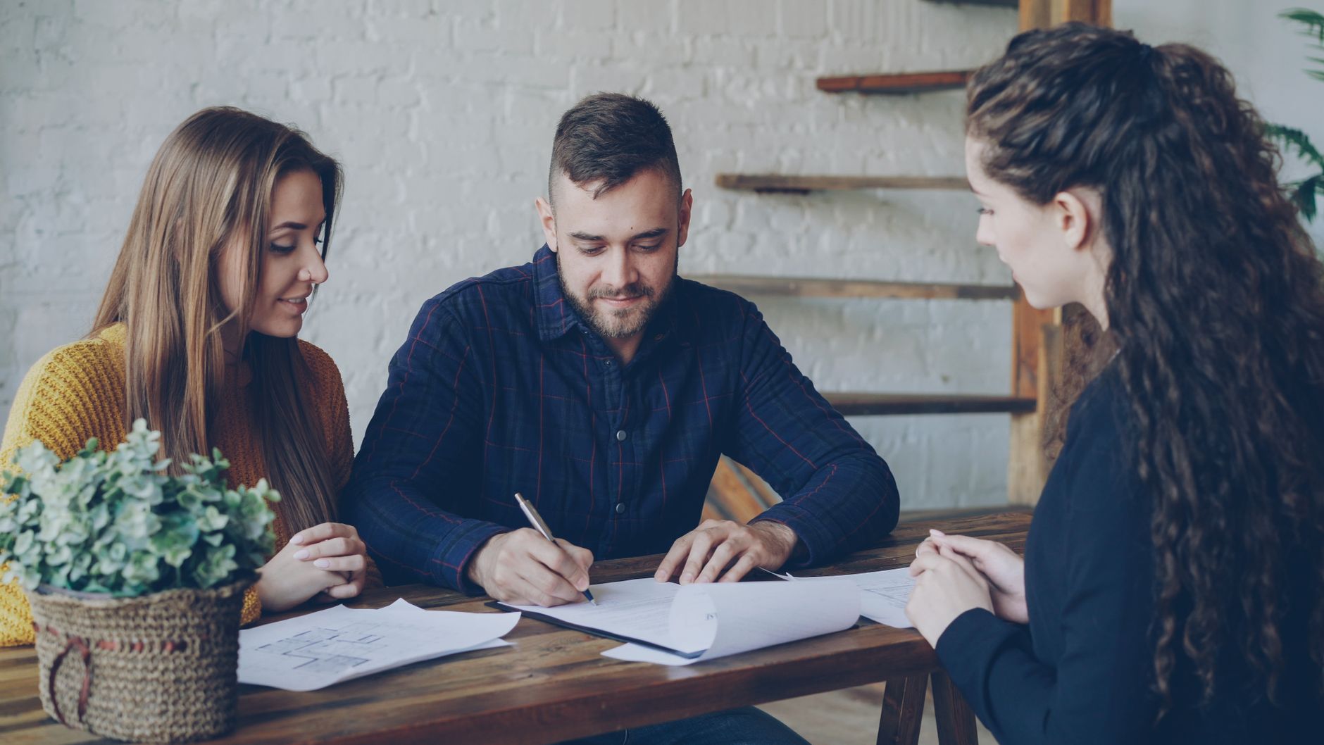 A young couple discussing paperwork with a real estate agent indoors.