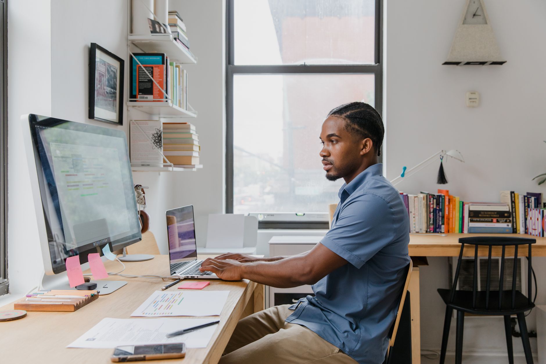 A professional man working on a laptop and computer in a stylish home office setting.