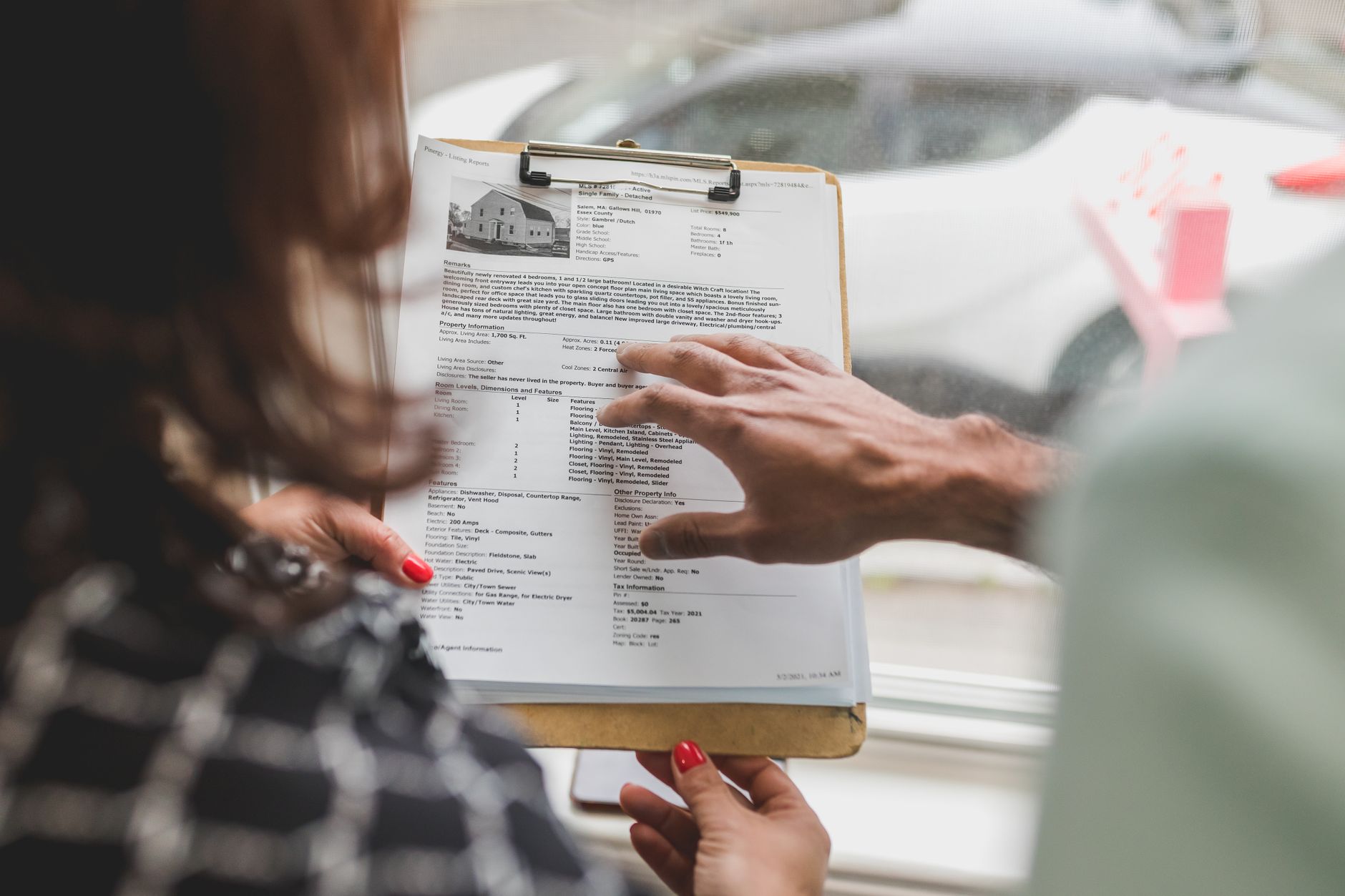 Real estate agent discussing property details with client using a clipboard indoors.